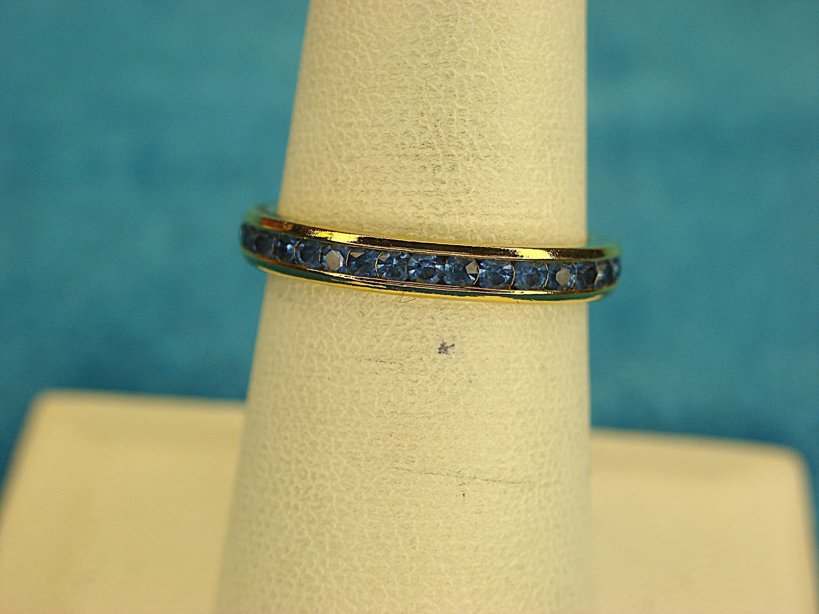 AVON GOLD TONE BAND RING WITH BLUE STONES ALL AROUND – SIZE 6 3/4